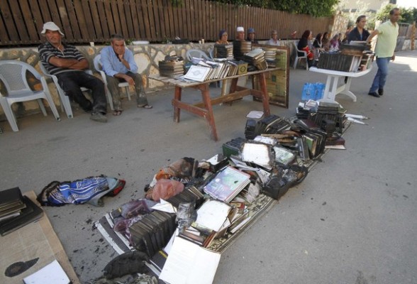 Residents sit next to damaged books outside a burnt mosque in the Bedouin village of Tuba Zangaria