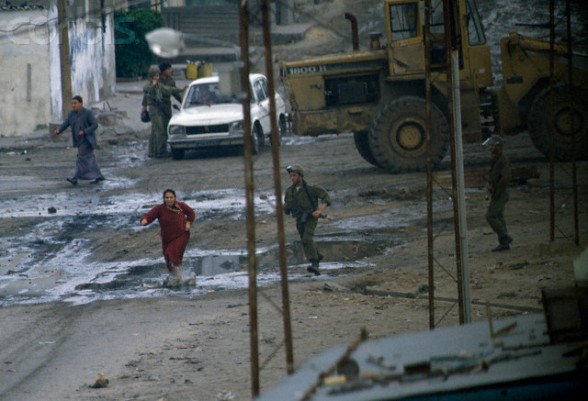 13 Feb 1988, Gaza, Gaza Strip --- A civilian Palestinian woman flees from armed soldiers in the streets of Gaza. Violence broke out after rebel Israeli and Palestinian fighters protested in the occupied territory of Gaza during the first Intifada. --- Image by Patrick Robert/Sygma/CORBIS