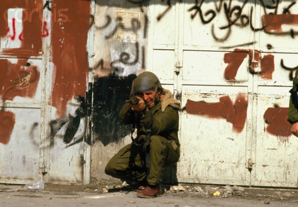19 Feb 1988, Nablus, West Bank --- A soldier aims his assault rifle at Palestinian demonstrators during a protest in the streets of Nablus after the Friday Prayer. Violence broke out after rebel Israeli and Palestinian fighters protested in the disputed territory of West Bank during the first Intifada. --- Image by Patrick Robert/Sygma/CORBIS