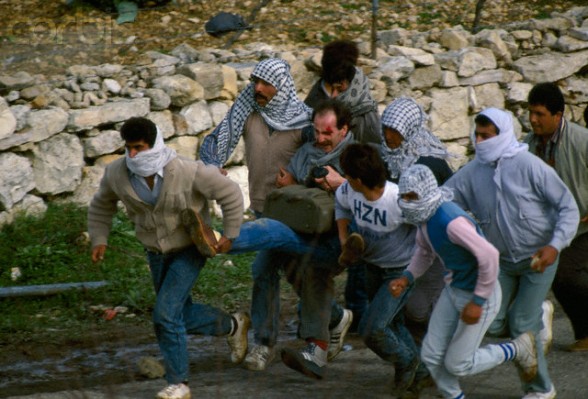 24 Feb 1988, Beit Ummar, West Bank --- Palestinian rebels carry a wounded photographer away from danger during a protest in the streets of Beit Omar. Violence broke out after rebel Israeli and Palestinian fighters protested in the disputed territory of West Bank during the first Intifada. | Location: Beit Omar, West Bank.  --- Image by Patrick Robert/Sygma/CORBIS