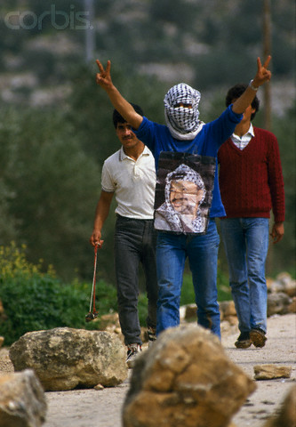 February 1988, West Bank --- A Palestinian demonstrator, wearing a poster of Palestinian Liberation Organization leader Yasser Arafat, gives the peace sign during an uprising. Violence broke out after rebel Israeli and Palestinian fighters protested in the disputed territory of West Bank during the first Intifada. --- Image by  Patrick Robert/Sygma/CORBIS