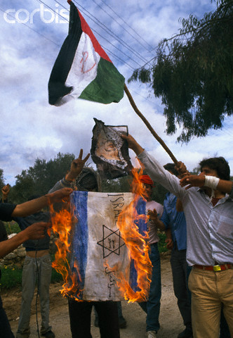 February 1988, West Bank --- Palestinian demonstrators burn the Israeli flag and wave the Palestinian Liberation Organization flag, outlawed by Israel, during an uprising. Violence broke out after rebel Israeli and Palestinian fighters protested in the disputed territory of West Bank during the first Intifada. --- Image by  Patrick Robert/Sygma/CORBIS