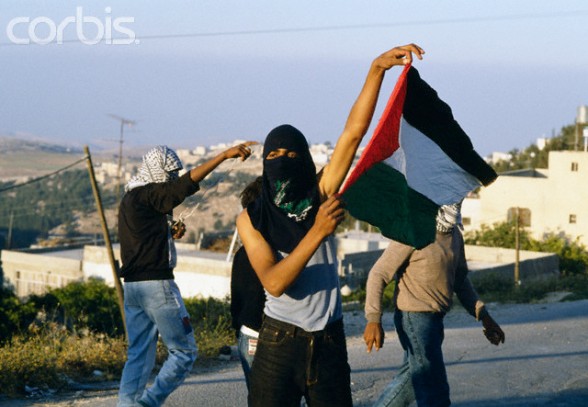 22 May 1990, Shu'fat, East Jerusalem, West Bank --- A masked Palestinian man holds up a Palestinian flag during a riot in Shufat, Jerusalem. The riot is in response to a shooting by a discharged Israeli soldier that occurred two days before in Rishon le-Ziyyon, which killed eight Palestinian laborers and wounded nine others. --- Image by Patrick Robert/Sygma/Corbis