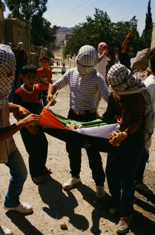 ca. 1989, Israel --- Masked children of the Intifada cradle rocks on a Palestine flag in preparation for a demonstration in the Kalandia Refugee Camp in the West Bank. | Location: Near Jerusalem, Israel.  --- Image by Ricki Rosen/CORBIS SABA