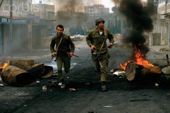 20 Jan 1988, West Bank --- Burning trash cans litter a village street in West Bank as Army soldiers run for cover during a riot in the Intifada. --- Image by Ricki Rosen/CORBIS SABA