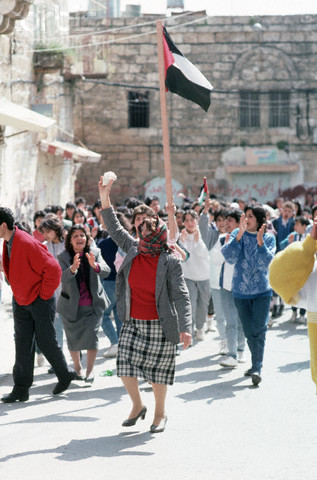 ca.1988 --- A woman marches in front of the outlawed Palestinian flag, holding a rock aloft, during the Intifada, in the West Bank town of Bet Sachour. | Location: Bet Sachour, Israeli Occupied Territories.  --- Image by David H. Wells/CORBIS