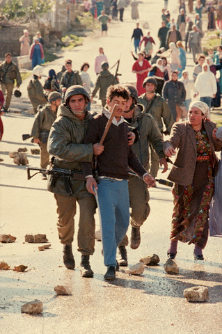 1988, West Bank --- Israeli soldiers escort an arrested man down a street littered with rocks thrown by Palestinian guerillas. --- Image by Peter Turnley/CORBIS